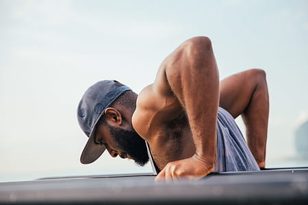 A bearded young African man wearing tank top and cap exercising on workout bars thumbnail