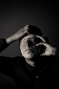 grayscale photography of man holding his face covered with mud thumbnail