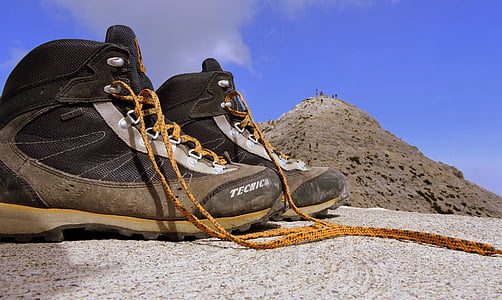 gray-and-brown hiking boots on gray sand overlooking brown hill under blue skies thumbnail