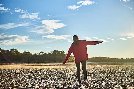 Woman in Red Sweater and Black Pants on White Sand Near Body of Water During Daytime thumbnail