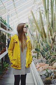 woman wearing black and white striped dress and yellow jacket staring at plant thumbnail
