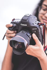 shallow focus photography of a woman holding black Canon EOS-1D camera thumbnail