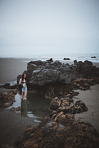 woman standing on body of water near rock thumbnail