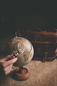 person using magnifying glass on white and blue desk globe thumbnail