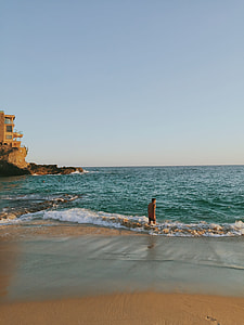 man in orange tank top and black shots outfit standing at blue sea during daytime thumbnail