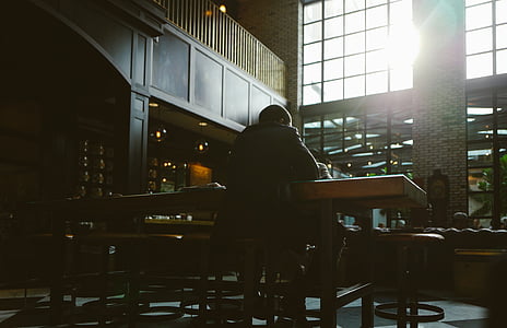 person sitting on chair leaning on brown table inside dark room thumbnail