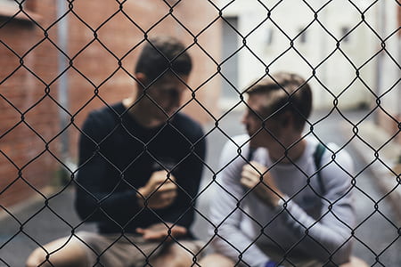 two men sitting down talking with gray chain fence infront thumbnail