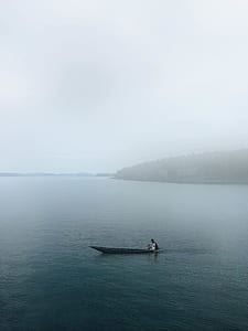 man riding boat on sea near mountain thumbnail