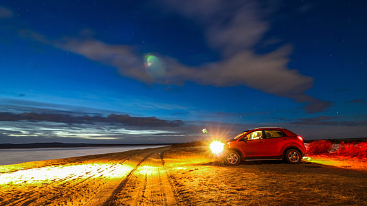 red SUV on sand bear body of water at night \ thumbnail