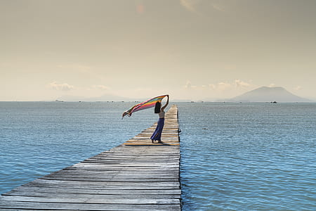 woman holding textile standing on gray wooden sea dock during daytime thumbnail
