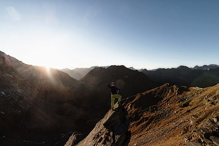 Man Standing on Rock on Top of Mountain Facing Sun thumbnail