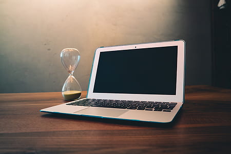 Computer Laptop Beside Hour Glass on Brown Wooden Surface thumbnail