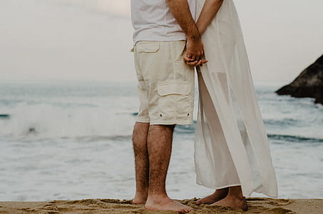 man and woman standing on seashore while holding hands during daytime thumbnail