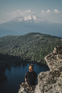 person sitting on gray rock near body of water at daytime thumbnail