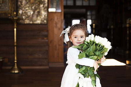 girl in white dress holding white roses bouquet inside a brown room thumbnail