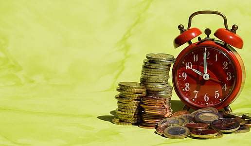 stack and pile of coins beside 2-bell alarm clock thumbnail