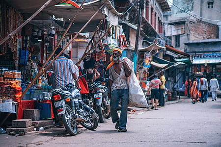 man carrying sack walking on street near stores thumbnail