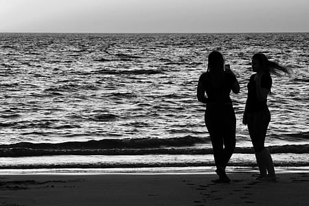 silhouette of two women standing on seashore under gray sky thumbnail