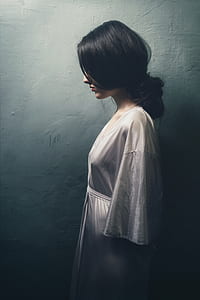 woman in white robe standing beside white concrete wall thumbnail