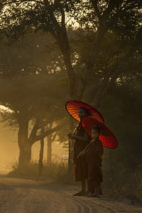 two boys holding red paper umbrellas standing beside tree looking towards thumbnail