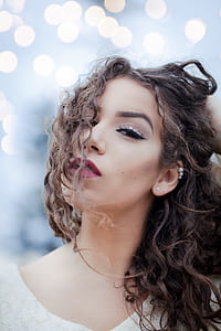 woman with black and brown curly hair wearing white pearl earrings holding her hair with one hand selective-focus photography thumbnail