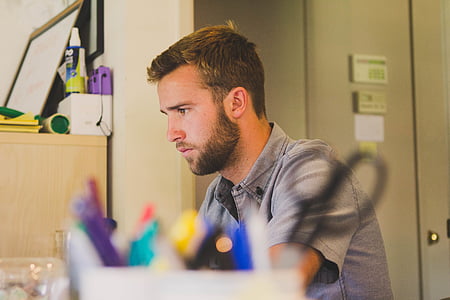 selective focus photography of man in gray shirt sitting in front of white desk thumbnail