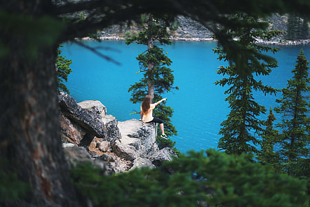 woman near body of water sitting on rock during daytime thumbnail