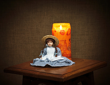 porcelain doll sitting near orange pillar candle thumbnail