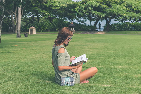 woman reading book while sitting on grass field thumbnail