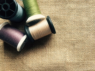 four assorted-color threads with spools over beige canvas textile thumbnail