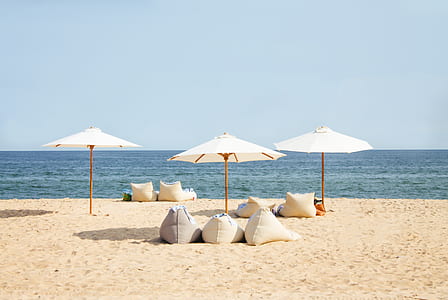 three white patio umbrellas on seashore thumbnail