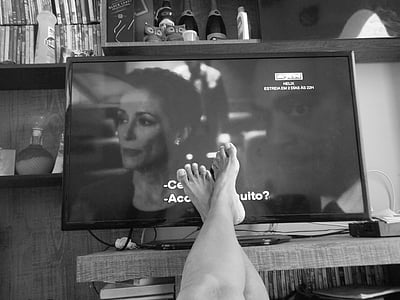 grayscale photo of person's feet in front of flat screen TV thumbnail