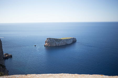A small rocky island surrounded by blue water with horizon in the background thumbnail