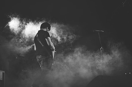 greyscale photo of man playing guitar near microphone thumbnail