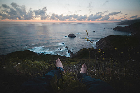 person sits on grass at the peak front of sea at daytime thumbnail