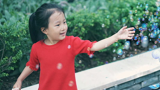 girl catching bubbles near plants at daytime thumbnail