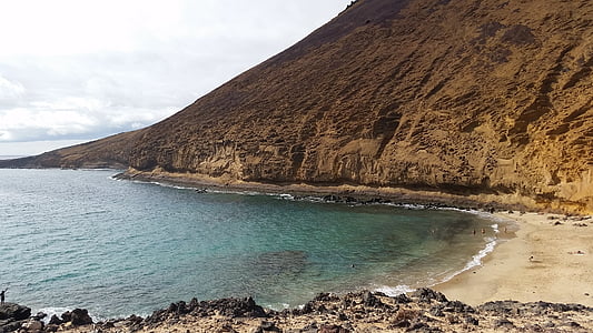 hill near body of water under white clouds and blue sky thumbnail