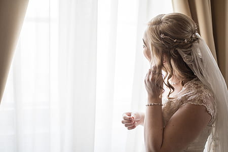 woman holding earring while looking window curtain thumbnail