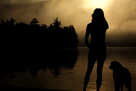 silhouette person standing beside dog near ocean thumbnail