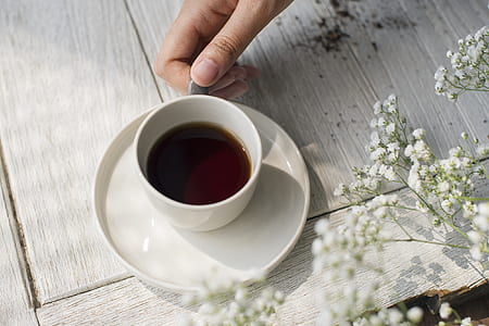 person holding white ceramic cup filled with brown liquid on saucer thumbnail