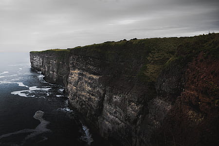 cliff beside body of water under gray sky thumbnail