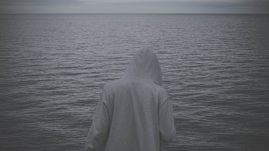 person in gray hoodie in front of body of water thumbnail