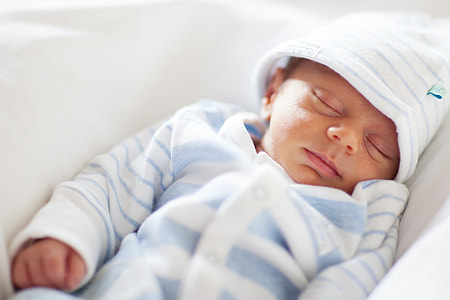 baby in white and blue footie pajama sleeping on the white textile thumbnail