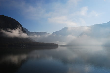 landscape photography of mountain near body of water surrounded with fogs thumbnail