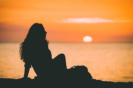 silhouette of woman sitting on seashore during sunset thumbnail