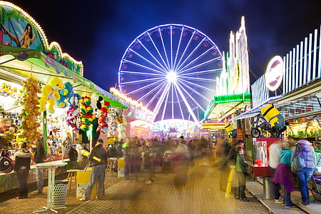 crowd of people standing and buying stuff at the carnival with ferris wheel background at night thumbnail