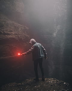 man in hooded jacket holding lighted flare in cave thumbnail
