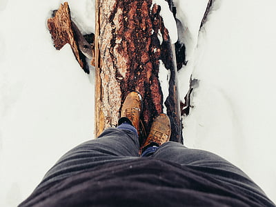 person wears black pants standing on brown tree log on snow field thumbnail