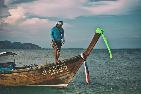 A man secures a longtail boat with rope in the Krabi district of Thailand thumbnail