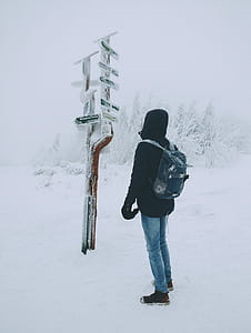 Person Wearing Black Hoodie and Blue Denim Jeans Standing over Frozen Arrow Signage over Snow Ground thumbnail
